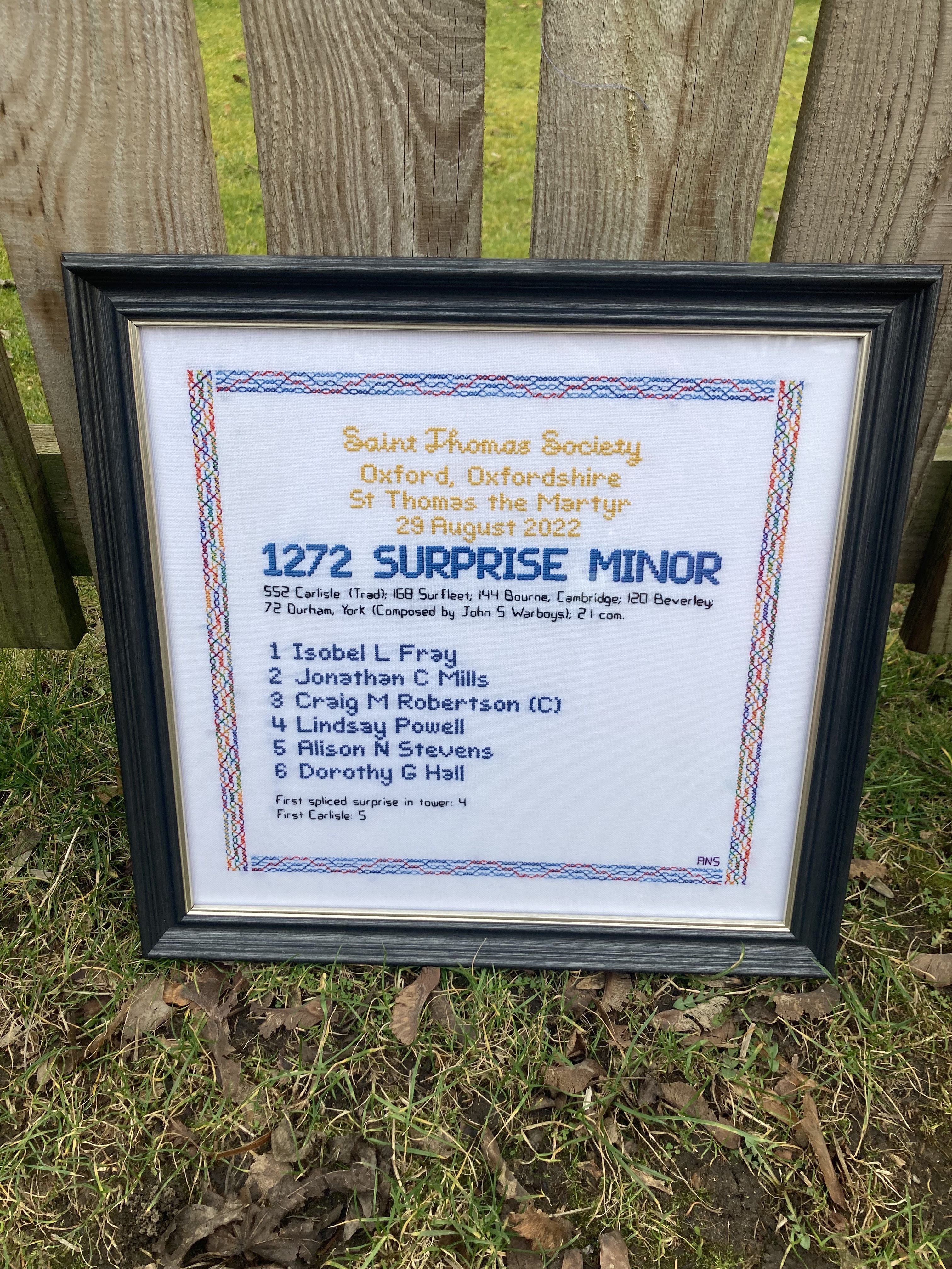 Embroidered quarter peal board framed leaning against a fence outside